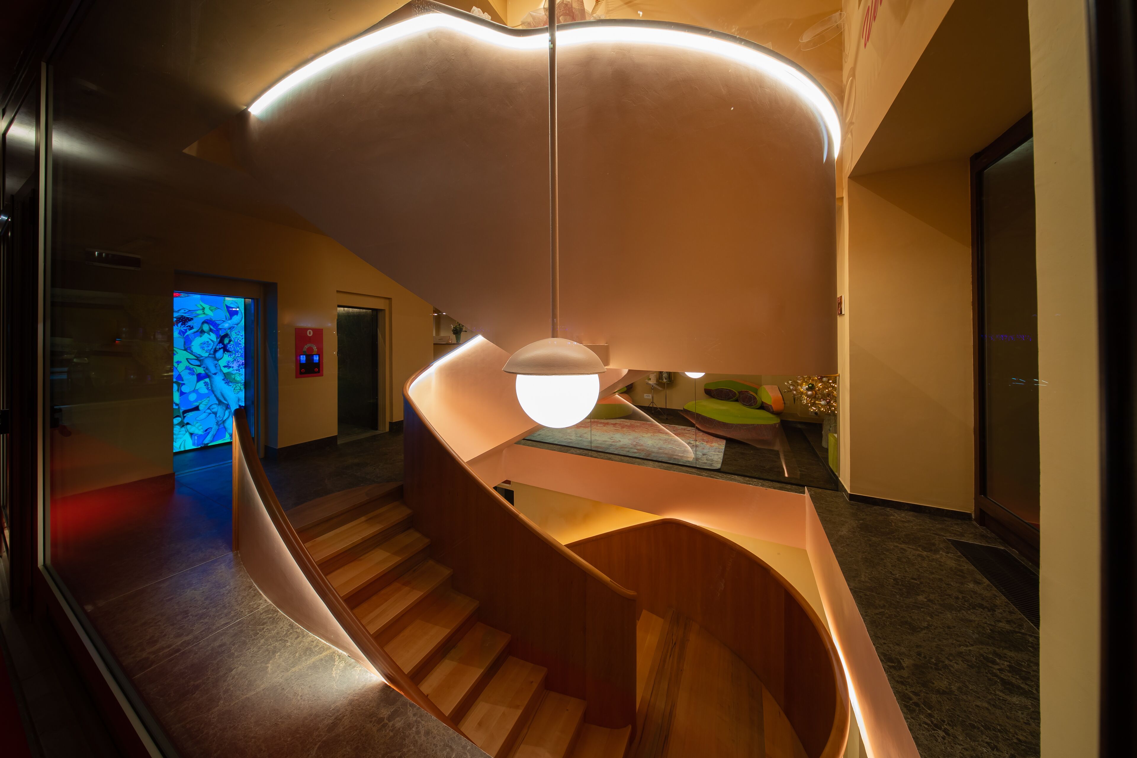Un interior moderno con una escalera curva, una exhibición de arte digital y una lámpara de techo única.