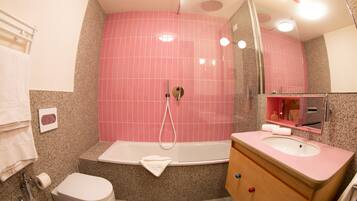 Un baño con pared de ducha en rosa, una bañera blanca, un mueble de tocador de madera con lavamanos rosa y un inodoro blanco.