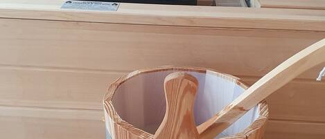 A wooden bucket with a metal band and a wooden spoon inside, placed on a wooden bench.