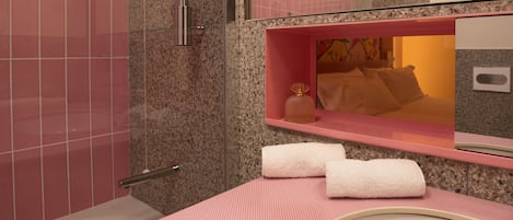 Un bagno con parete piastrellata in rosa, un piano di lavoro in granito, un lavandino bianco, uno specchio e un portascope.