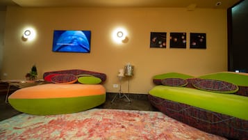 Una habitación moderna con un televisor de pantalla plana grande, dos luces empotradas, un tapete estampado y coloridos sillones de felpa.