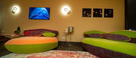 Una habitación moderna con un televisor de pantalla plana grande, dos luces empotradas, un tapete estampado y coloridos sillones de felpa.
