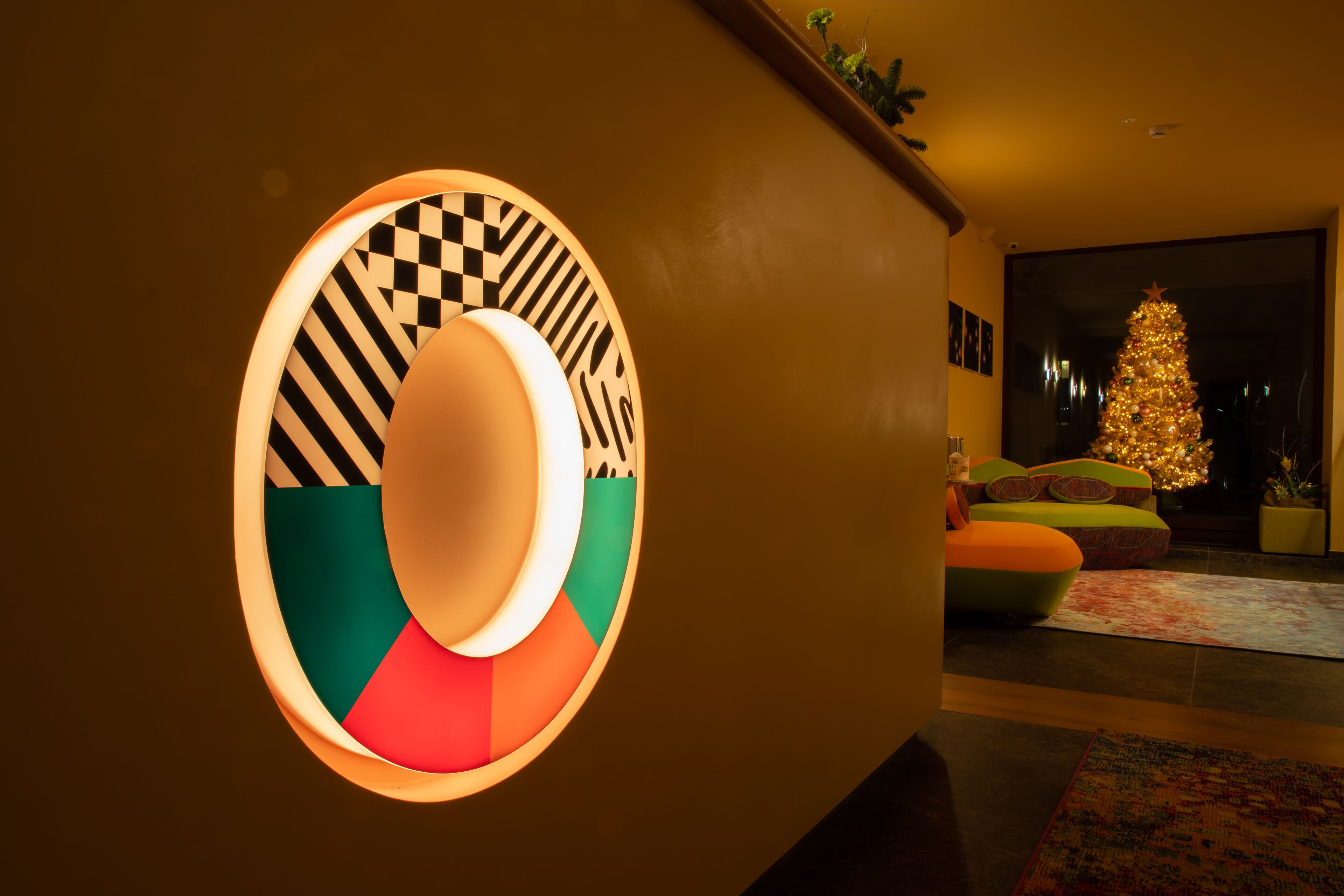 A modern interior with a circular wall feature, a Christmas tree, and colorful seating.