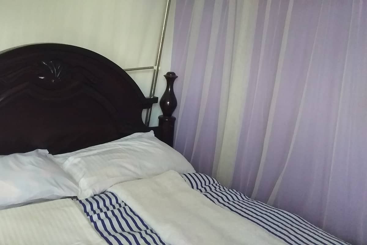 Cama com cabeceira escura, almofadas brancas e roupa de cama listrada.