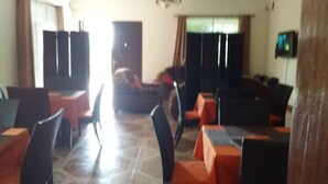 Un área de comedor con mesas y sillas, un sofá y un televisor en la pared.