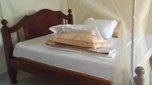 Una cama con cabecera de madera, ropa de cama blanca y una mosquitera.