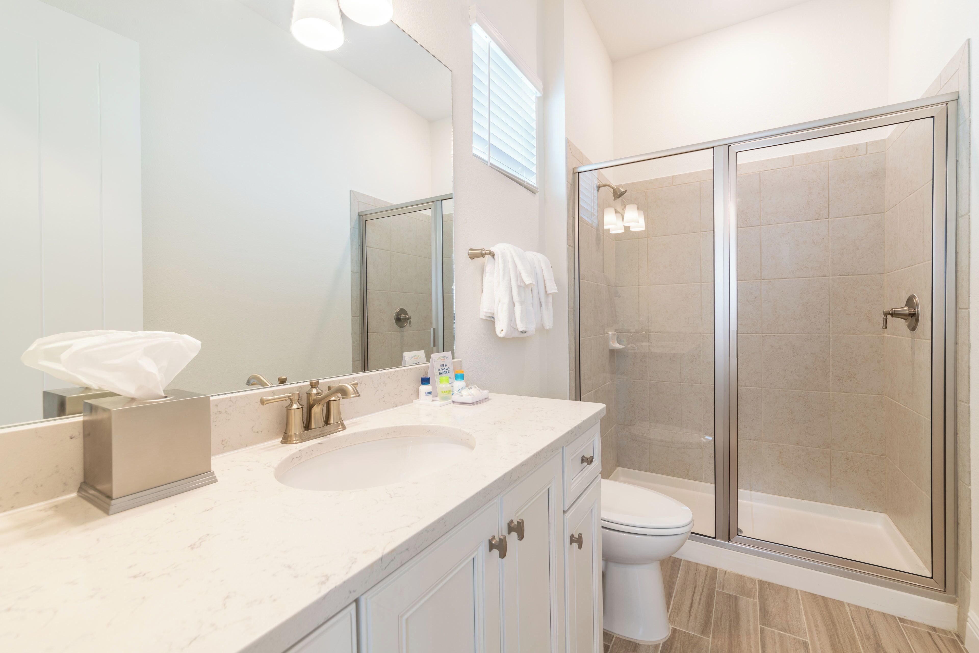 Un baño moderno con un espejo grande, un lavamanos, un inodoro y una ducha con mampara de vidrio.