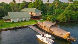 A house with a dock extending into a body of water, a boat moored at the dock, and lush greenery surrounding the property. - Cyrus Resort by Tolins Hotels & Resorts (Cherthala)