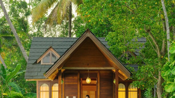 A wooden house with a porch, surrounded by lush greenery. - Cyrus Resort by Tolins Hotels & Resorts (Cherthala)