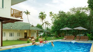 A swimming pool with lounge chairs and umbrellas, surrounded by lush greenery and a building with a balcony. - Cyrus Resort by Tolins Hotels & Resorts (Cherthala)