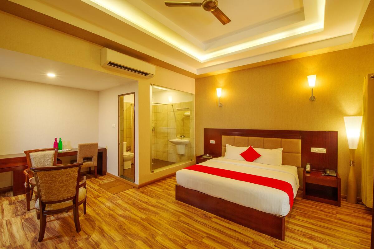 Ein Hotelzimmer mit Bett, Nachttisch, Sessel, Schreibtisch und einem Badezimmer mit Duschkabine.