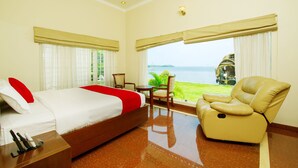 A hotel room with a bed, a chair, a table, and a view of the sea. - Cyrus Resort by Tolins Hotels & Resorts (Cherthala)