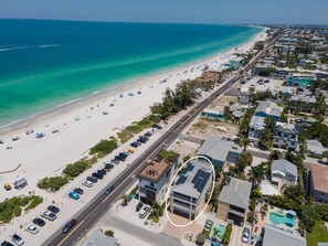 An aerial view of a coastal area with a beach, a road, and residential buildings.