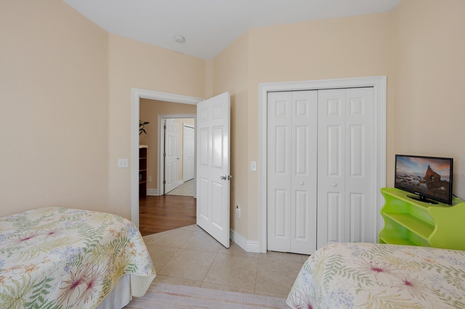 A bedroom with two beds, a television on a stand, and a door leading to another room.