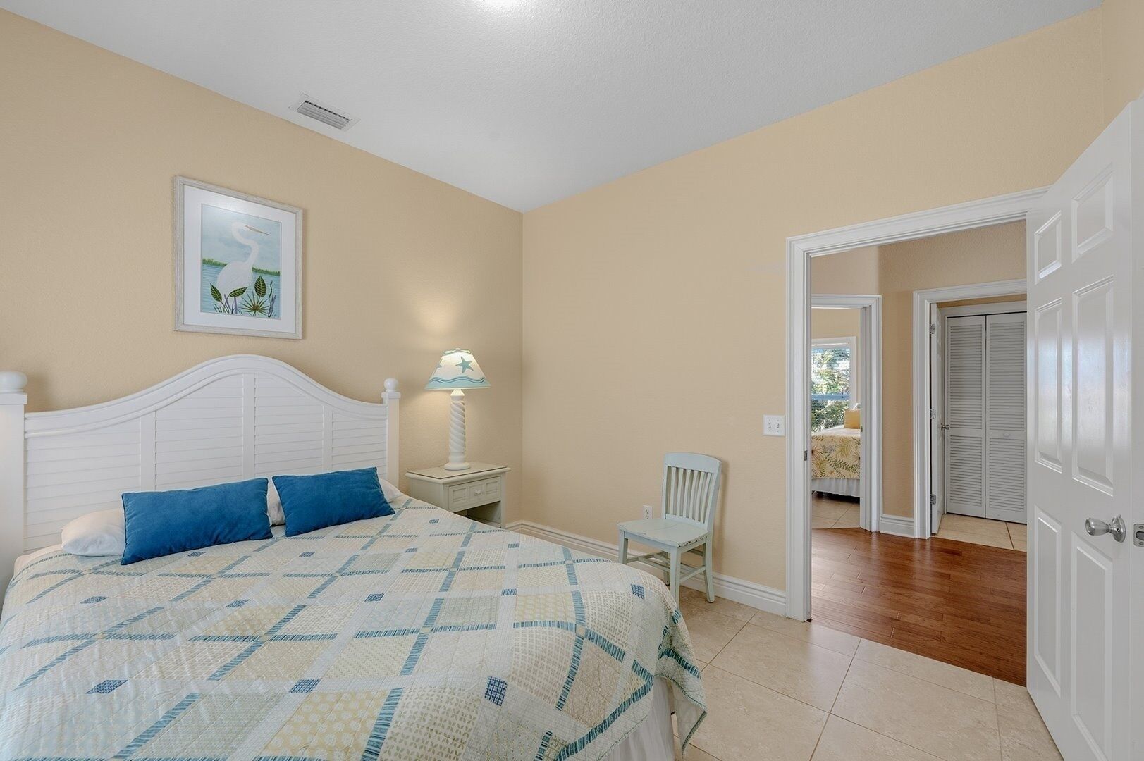 A bedroom with a bed, a nightstand, a chair, and a door leading to another room.
