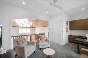 A modern living room with a ceiling fan, two sofas, a small round table, and a kitchen area with wooden cabinets. - Dockside Darling 3 Bedroom Home by RedAwning (Bradenton Beach)