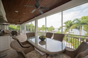 A covered outdoor dining area with wicker furniture, a glass table, and a view of the water. - Dockside Darling 3 Bedroom Home by RedAwning (Bradenton Beach)