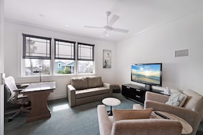 Ein modernes Wohnzimmer mit einem großen Fenster, einem Flachbildfernseher, einem Deckenventilator und einer Sitzecke mit Couchtisch.