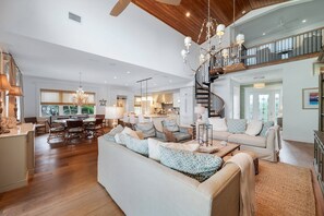 A spacious living room with a large sofa, dining area, kitchen, and a staircase leading to an upper level. - Dockside Darling 3 Bedroom Home by RedAwning (Bradenton Beach)