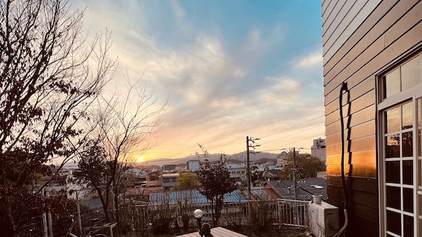 Terrassa exterior amb dues cadires de fusta i una taula, amb vista a un paisatge urbà al capvespre.