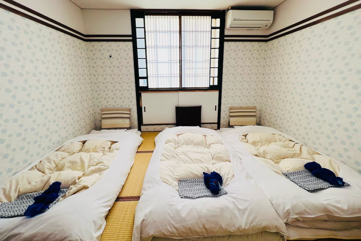 Habitación con dos camas, una ventana con rejas, aire acondicionado y pared con estampado.