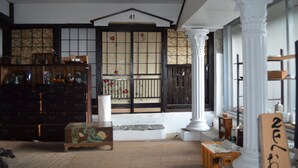 Une pièce de style japonais traditionnel, avec un sol recouvert de tatamis, une porte coulissante en papier de riz (shoji) et une commode en bois contenant divers objets.