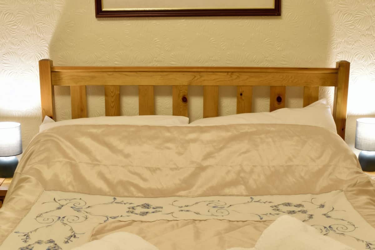 A neatly made bed with a floral bedspread, two folded towels, and a wooden headboard.