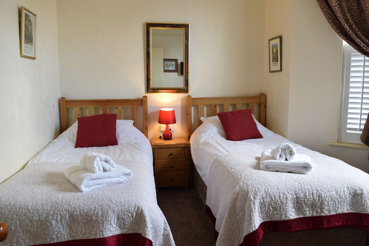 A double room with two beds, each with a red pillow and a white duvet. There is a nightstand with a red lamp between the beds.