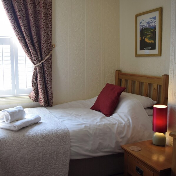 A neatly made bed with white linens and a red pillow, a wooden nightstand with a lamp, and a framed picture on the wall. - Bewdley Hill House (Kidderminster)