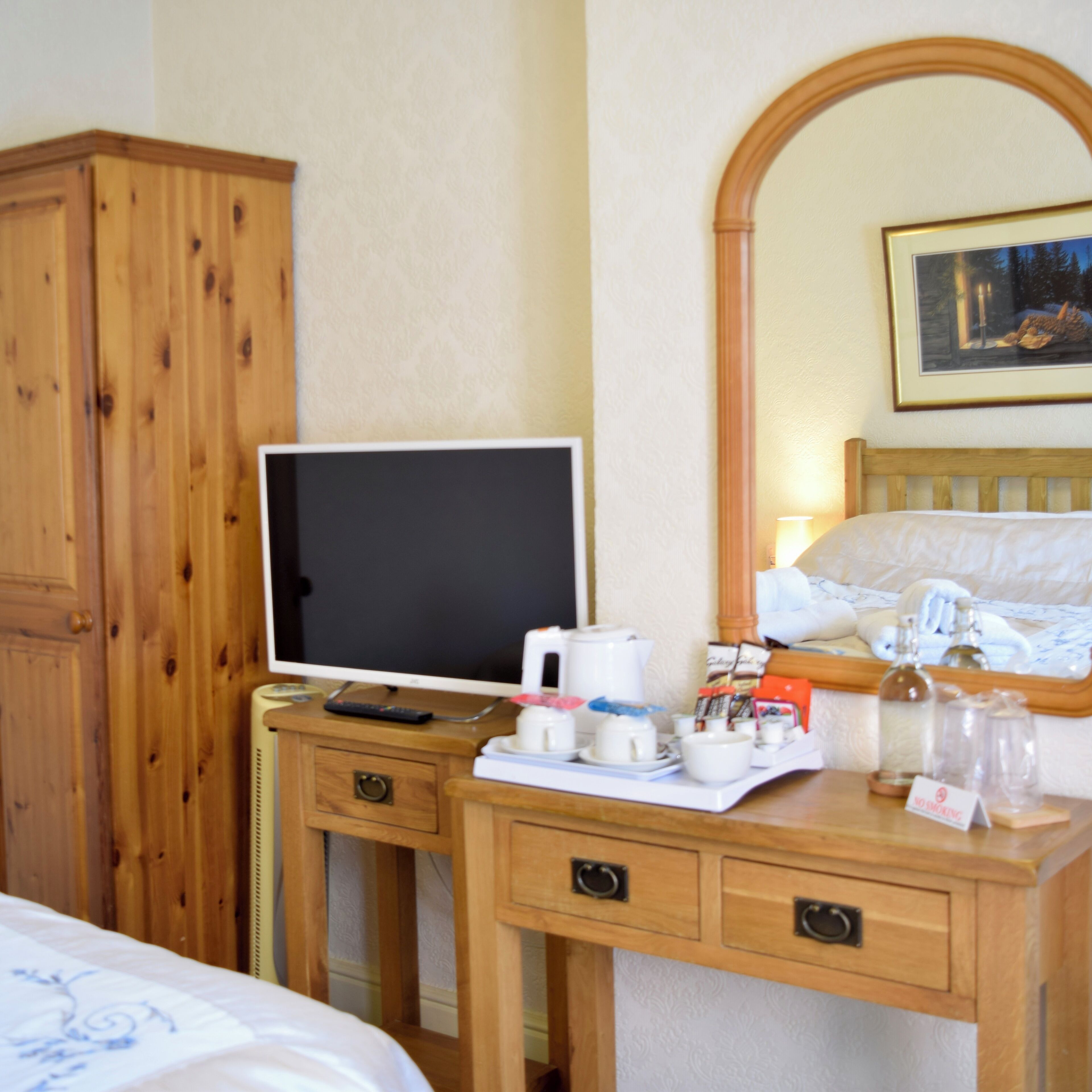 Una camera d'albergo con una scrivania in legno, una televisione, un letto e un quadro appeso al muro.