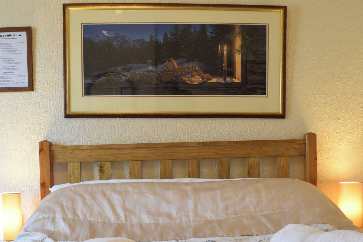 A neatly made bed with white linens and towels, a framed painting of a snowy landscape above it, and a wooden headboard.