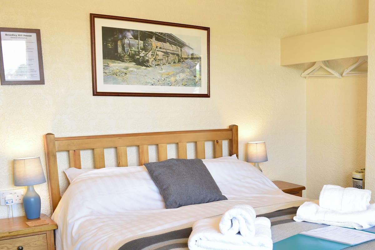 A neatly made bed with a striped blanket, two pillows, and a folded towel on a wooden headboard.