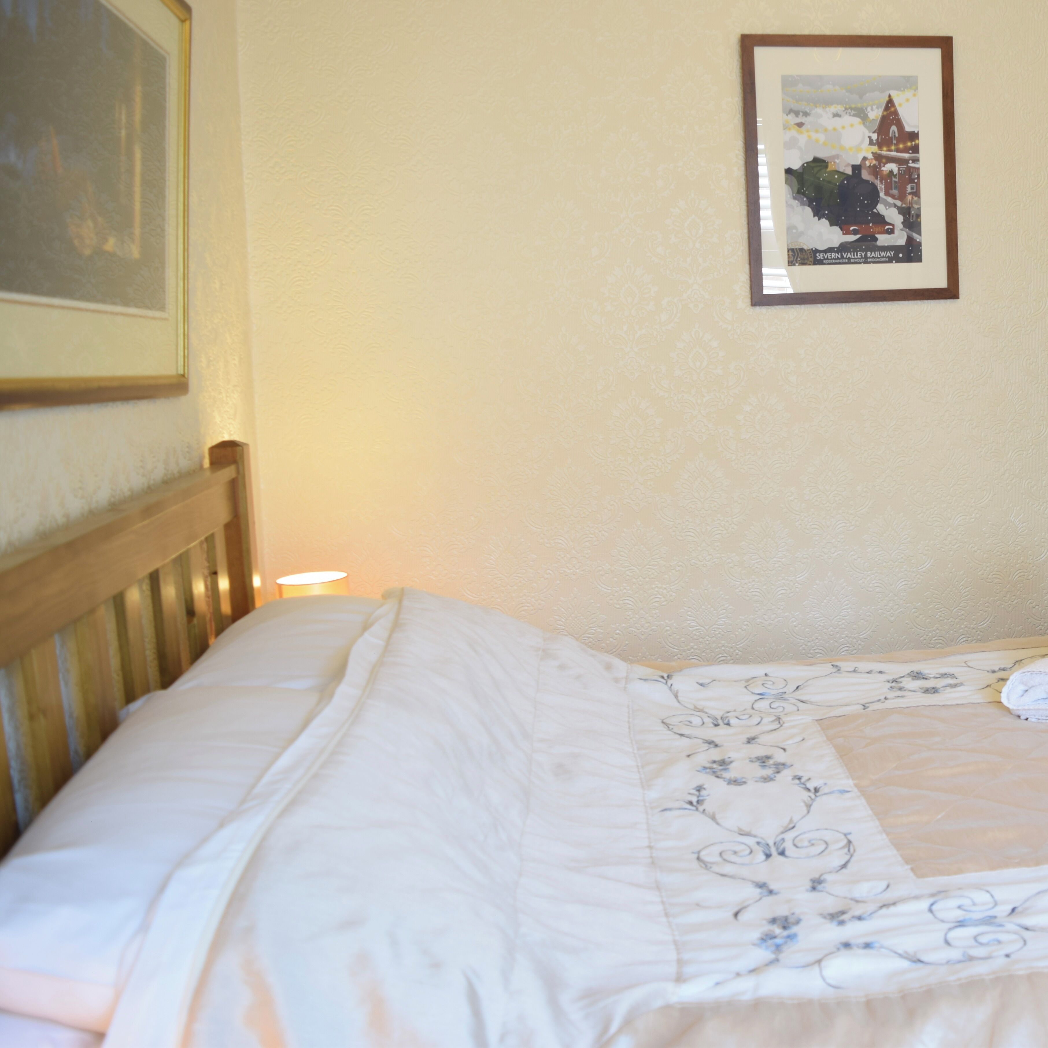 Un letto rifatto con cura, una coperta a motivi floreali, un quadro con un treno appeso alla parete e una lampada sul comodino.