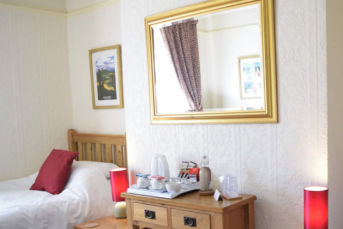 A hotel room with a bed, a wooden desk with drawers, a mirror, and two bedside lamps.