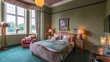 A traditional bedroom with a large bed, two bedside tables with lamps, a chair, and a window with curtains.