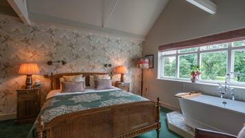 Un dormitorio con una cama grande, dos lámparas de noche, una ventana con vistas a zonas verdes y un baño separado con bañera y lavamanos.