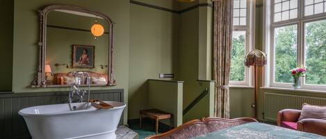 Une chambre traditionnelle avec une grande baignoire, un lit recouvert d’une courtepointe à motifs, un miroir et une fenêtre avec des rideaux.