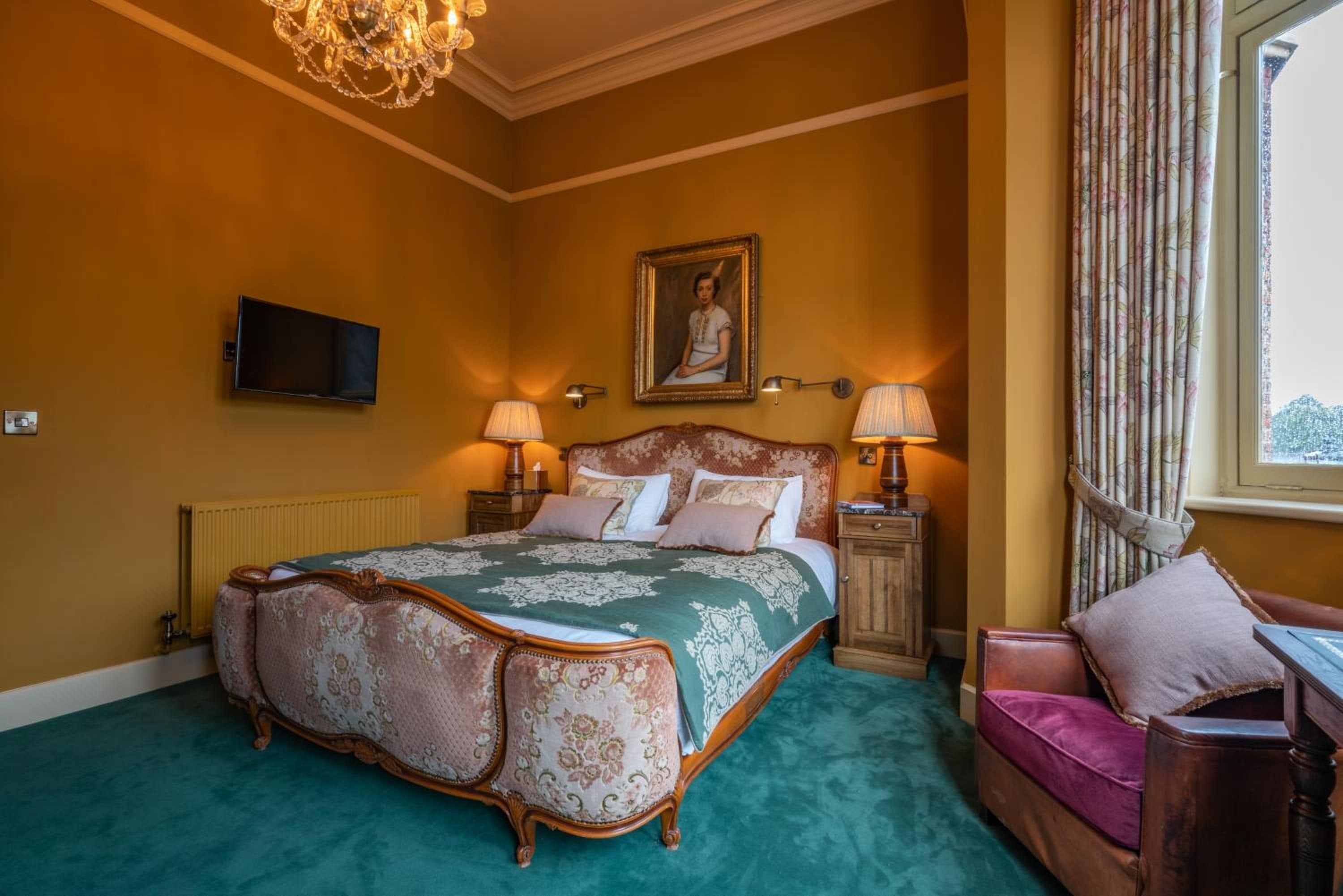 A bedroom with a large bed, two bedside lamps, a television on the wall, and a window with curtains.