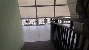 A staircase with a metal railing, leading to a balcony with a view through a window with a mesh screen. - Senevin Gardens Hotel (Kabwohe)