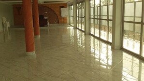 A spacious lobby with a polished marble floor, large windows, and a brick wall with a whiteboard. - Senevin Gardens Hotel (Kabwohe)
