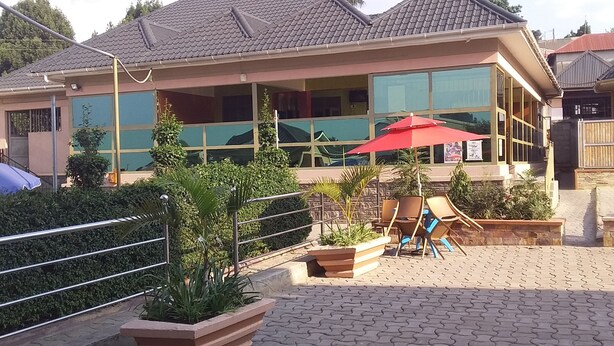 A building with large windows, outdoor seating, and a red umbrella. - Senevin Gardens Hotel (Kabwohe)