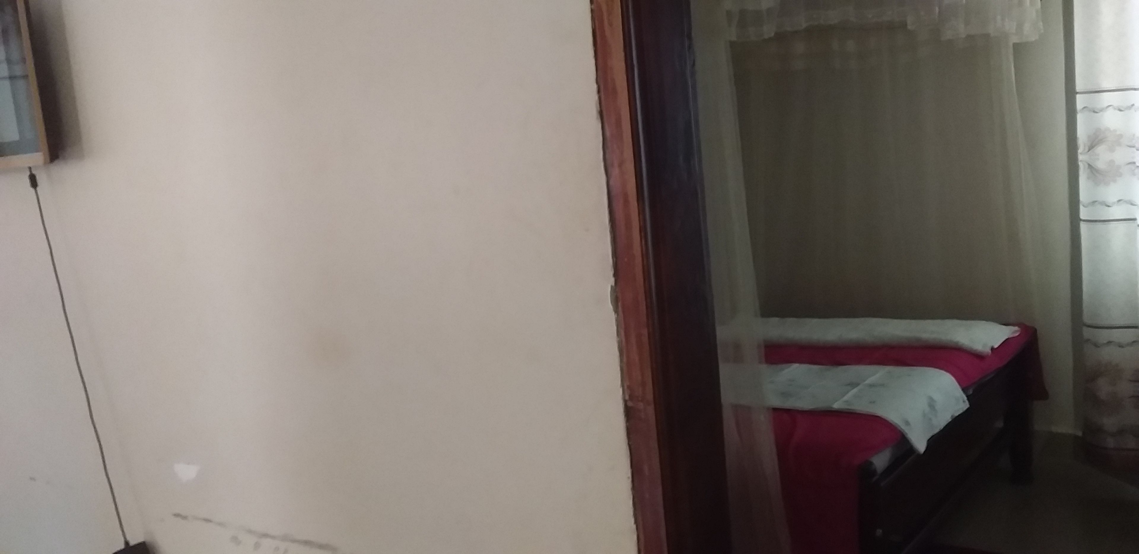 Une pièce avec un lit, une fenêtre avec un rideau et une prise électrique au mur.