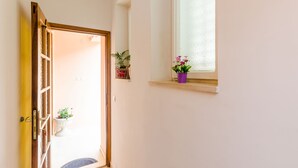 Een gang met een houten deur, een klein raam met een bloempot en een lichtschakelaar op de muur.