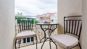 Een balkon met twee stoelen en een tafeltje, met uitzicht op een rij huizen met rode daken.