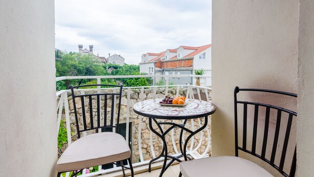 Een balkon met een ronde tafel en twee stoelen, een stenen muur en uitzicht op gebouwen en groen.