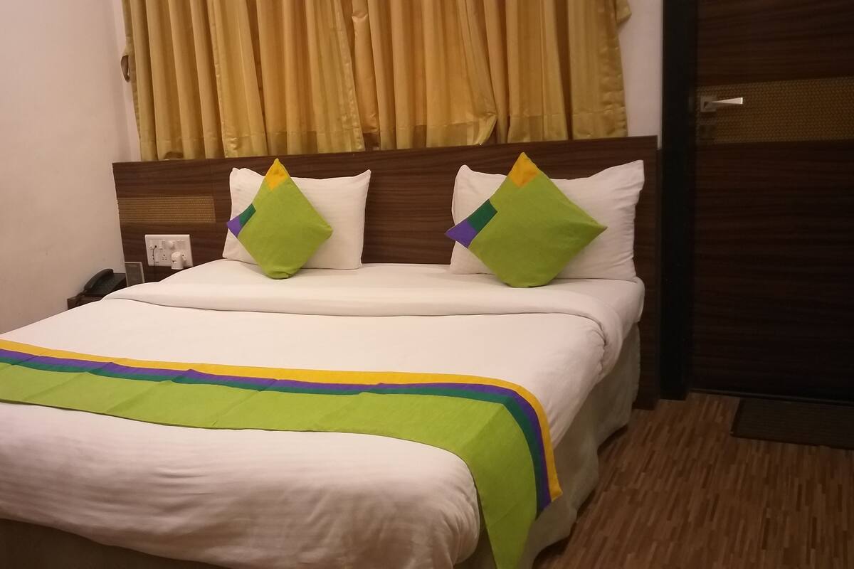 A neatly made bed with a white comforter and a green and yellow striped blanket. There are two pillows with green and yellow accents. The room has wooden flooring and a wooden headboard.