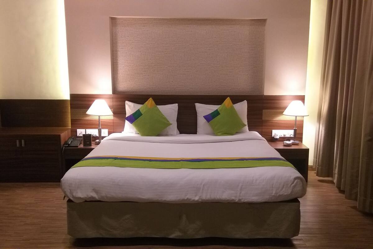 A hotel room with a large bed, two bedside lamps, a telephone, and a window with curtains.