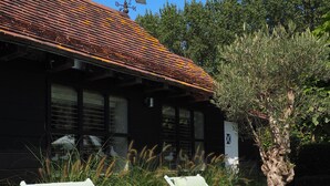 Deux fauteuils de jardin, un arbre en pot et un bâtiment surmonté d’un coq girouette.