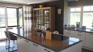 Une cuisine moderne dotée d’un grand îlot central, de tabourets de bar, d’un four encastré et offrant une vue sur l’extérieur.