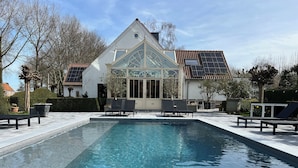 Une piscine avec des chaises longues, une véranda et des panneaux solaires sur le toit.